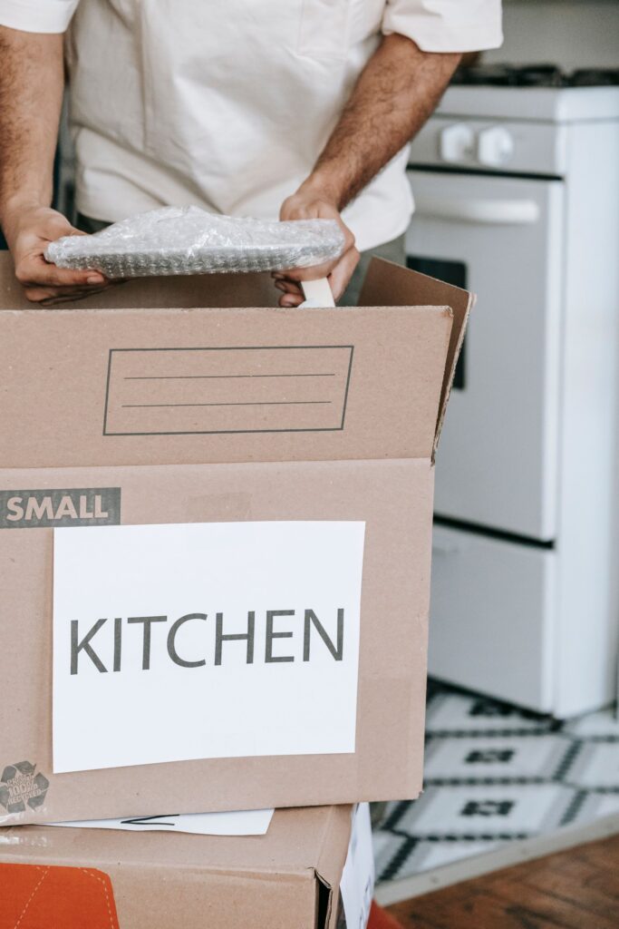 Ein Mann verpackt Küchengeschirr in einen Karton mit der Aufschrift „Kitchen“.